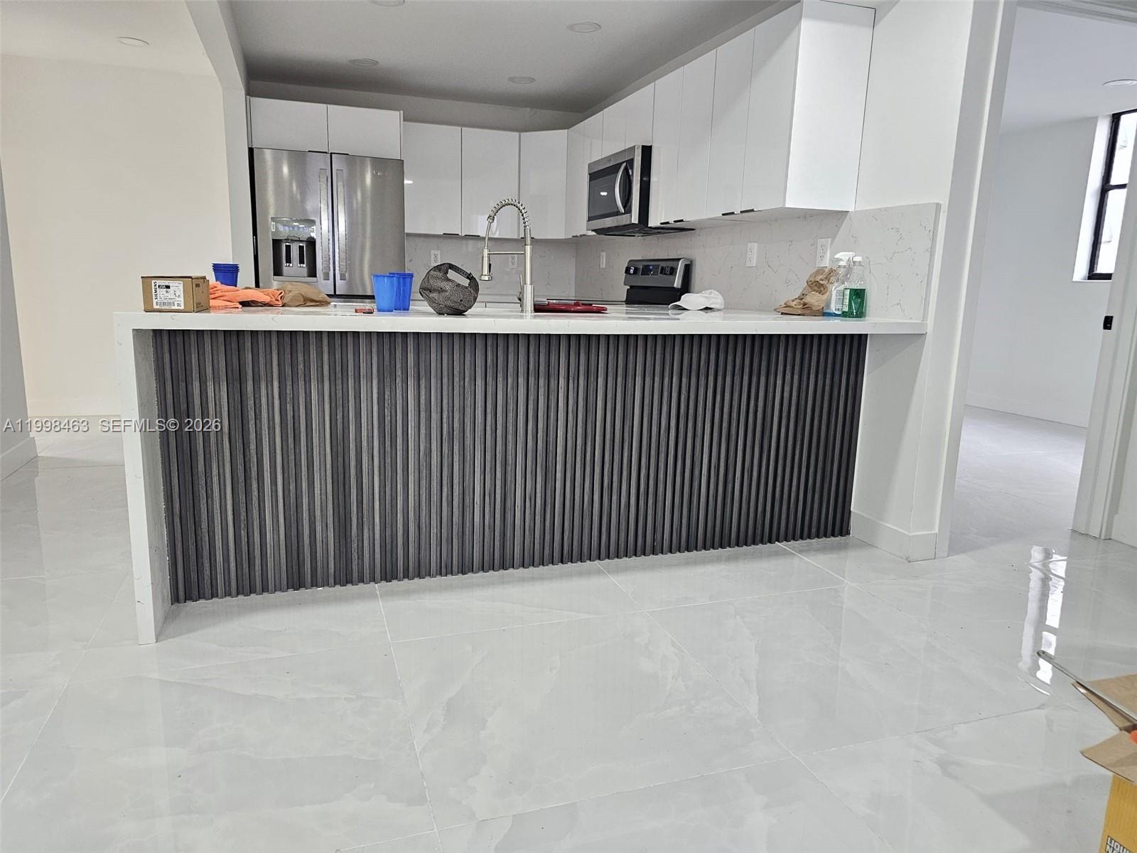 A modern kitchen features white cabinets, a stone countertop, and a dark, slatted wood island — 7125 Bay Dr # 506, Miami Beach FL 33141, MIAMI BEACH, FL