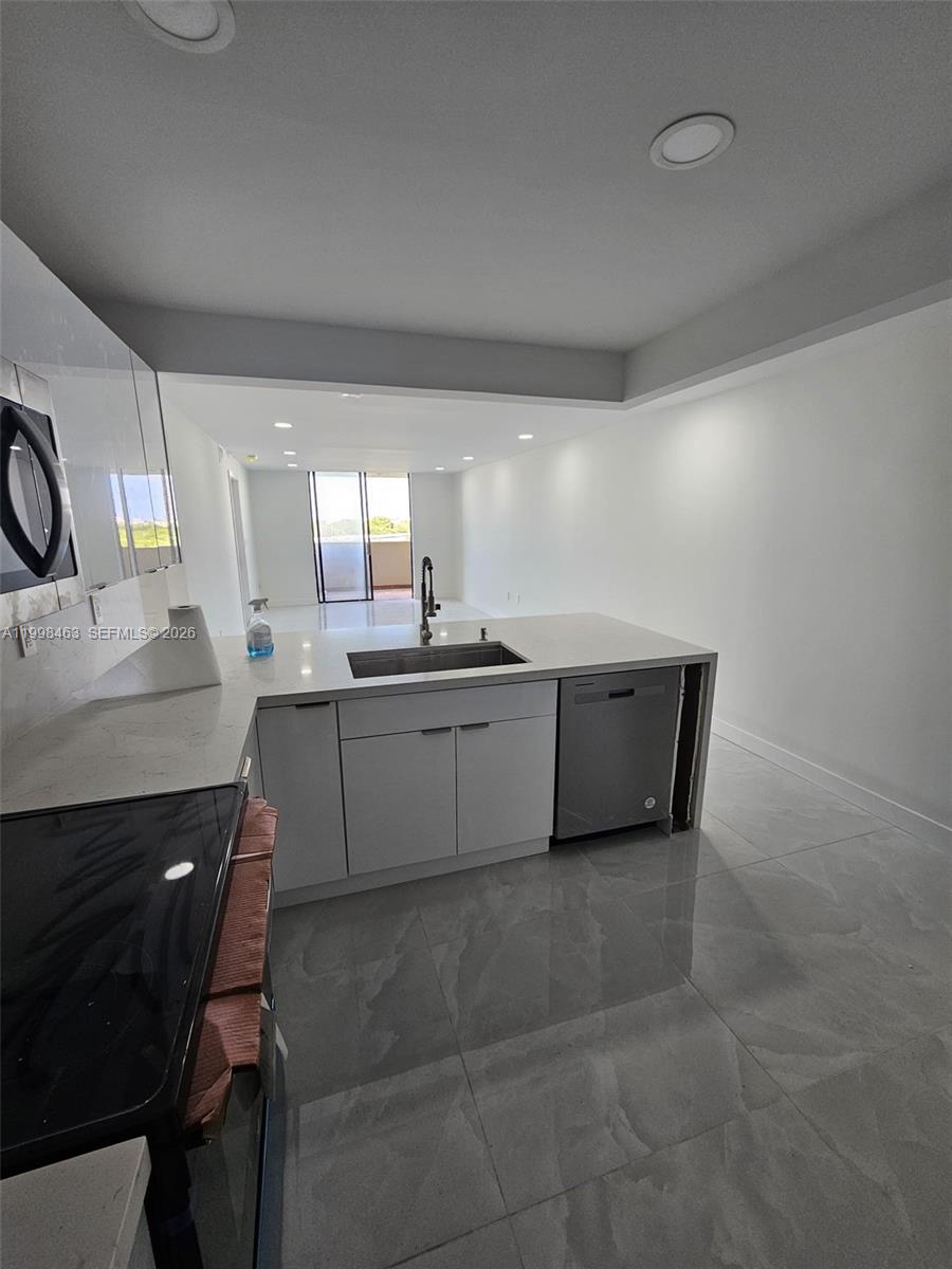 A modern kitchen features white cabinets, quartz countertops, a stainless steel dishwasher, and tile flooring — 7125 Bay Dr # 506, Miami Beach FL 33141, MIAMI BEACH, FL
