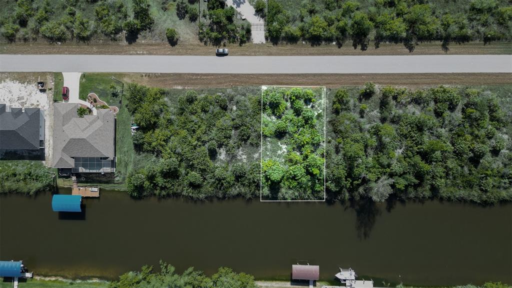 An aerial view shows a vacant, rectangular waterfront lot outlined in white between wooded properties — 15480 ARIBE AVENUE, PORT CHARLOTTE, FL