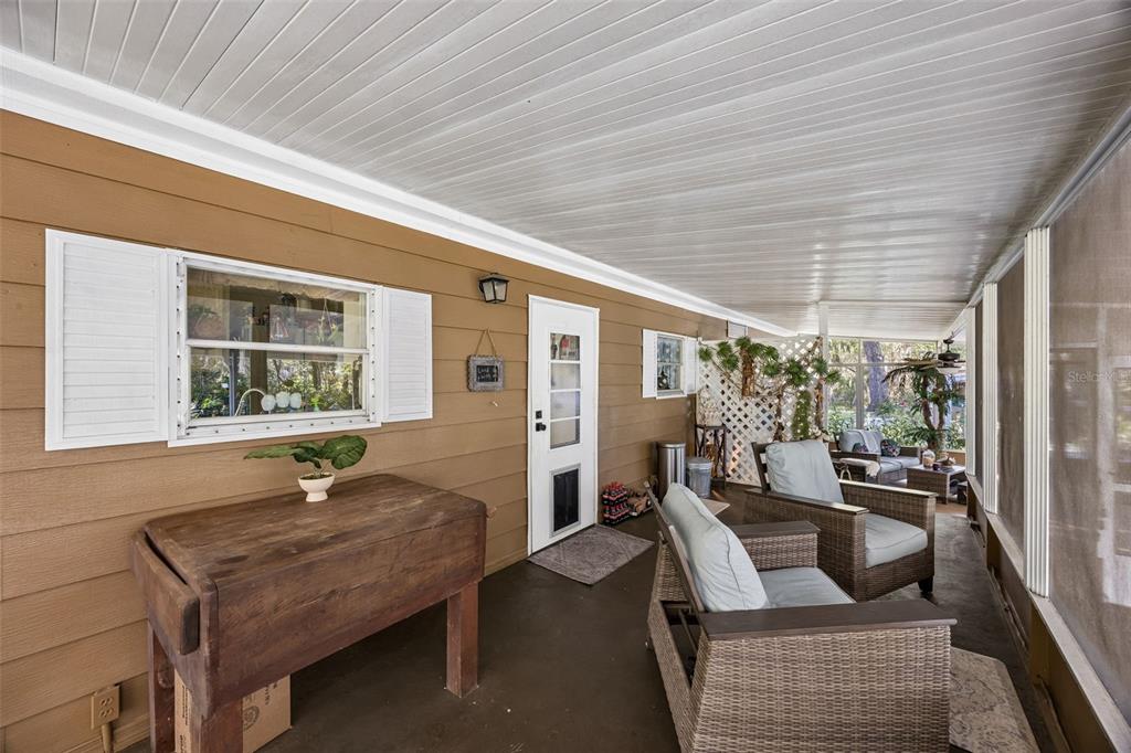 A covered porch features brown siding, a wooden table, and two wicker chairs with cushions — 110 PLUMOSA DRIVE, GEORGETOWN, FL