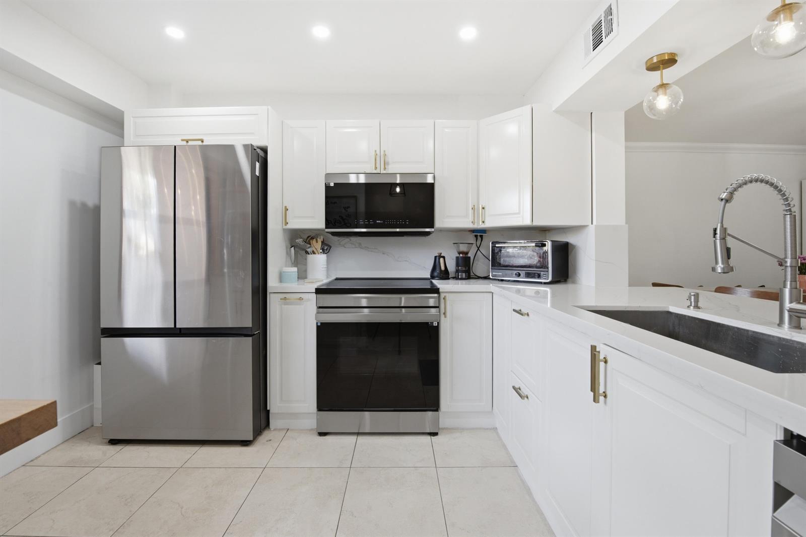 A modern kitchen features white cabinets, stainless steel appliances, and white quartz countertops — 371 W Park Drive # 17, Miami FL 33172, MIAMI, FL