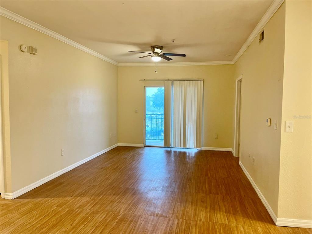An empty living room features wood-look flooring, a ceiling fan, and a sliding glass door — 5550 P G A BOULEVARD UNIT 5126, ORLANDO, FL