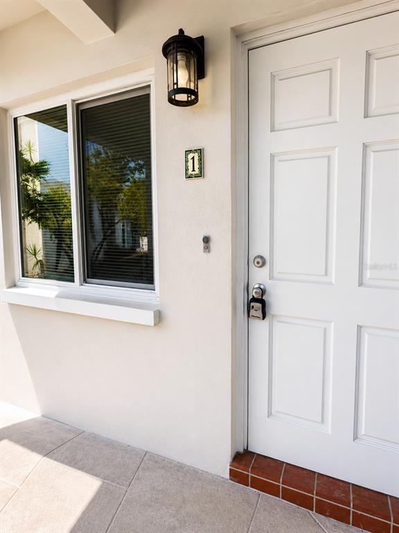 A white door with a lockbox and a window with blinds on a tiled porch — 295 110TH AVENUE UNIT 1, ST PETERSBURG, FL