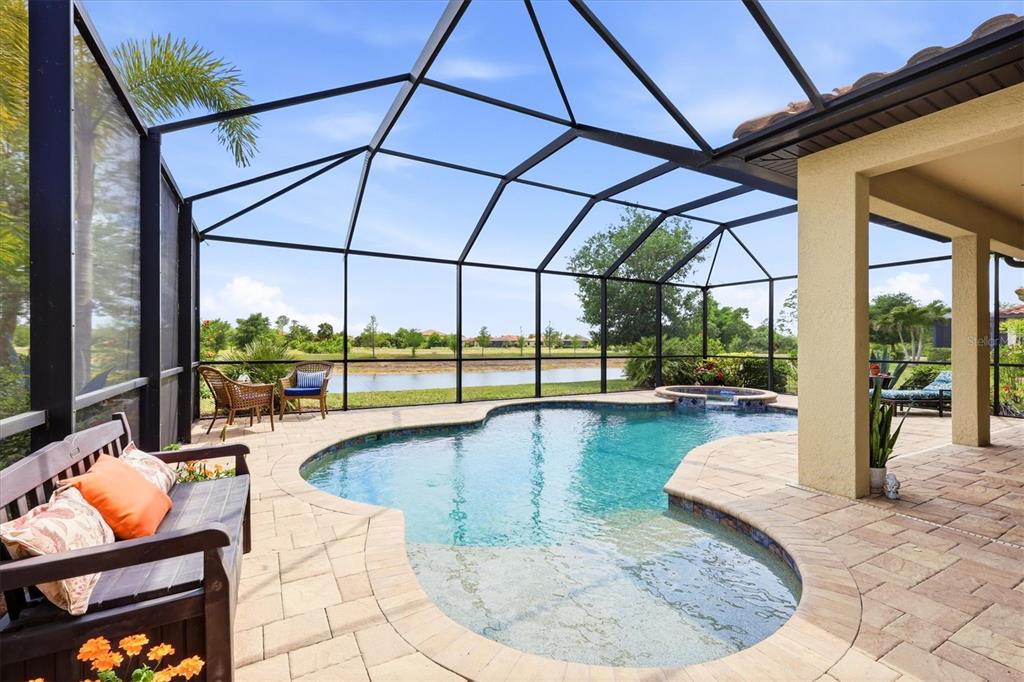 A screened-in pool patio features a kidney-shaped pool, a spa, and views of a lake — 12541 CINQUETERRE DRIVE, VENICE, FL
