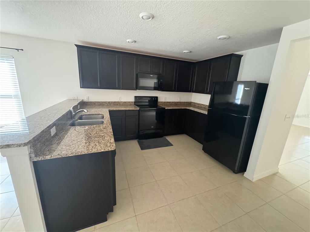 A kitchen features dark cabinets, granite countertops, a black refrigerator, and tile flooring — 6909 CRESTED ORCHID DRIVE, BROOKSVILLE, FL
