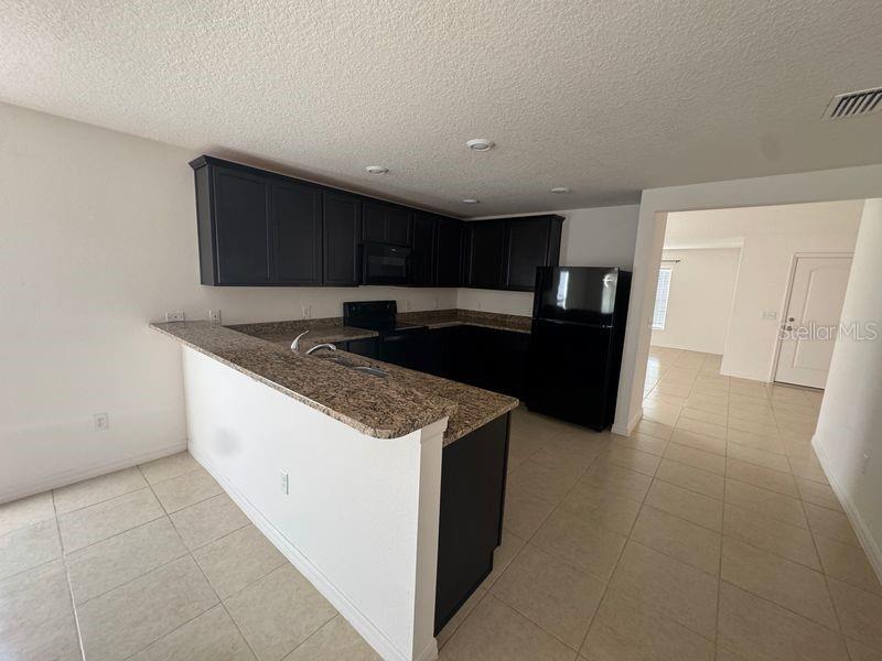 A kitchen features dark cabinets, granite countertops, and black appliances with tile flooring — 6909 CRESTED ORCHID DRIVE, BROOKSVILLE, FL