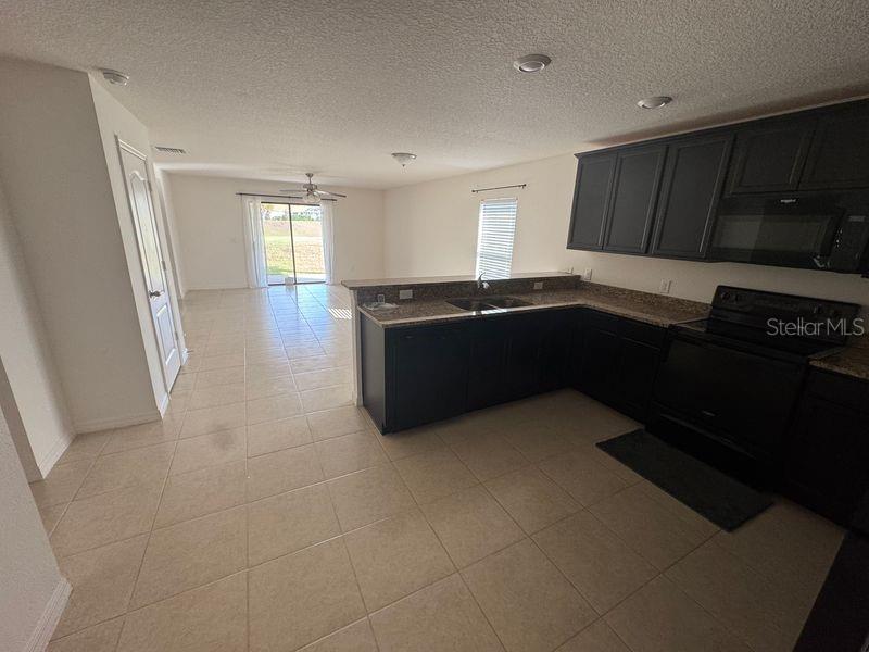 A kitchen with dark cabinets and tile flooring opens to a living area with sliding doors — 6909 CRESTED ORCHID DRIVE, BROOKSVILLE, FL