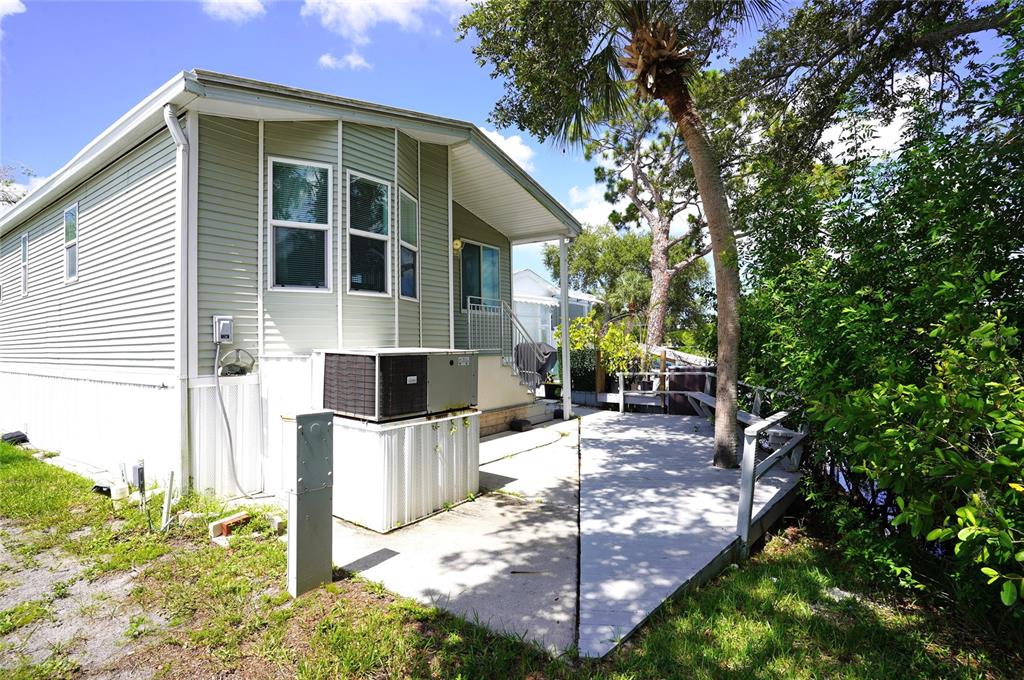 A light green mobile home features a concrete patio and a deck with a tree — 125 BROOKSHIRE DRIVE, NOKOMIS, FL