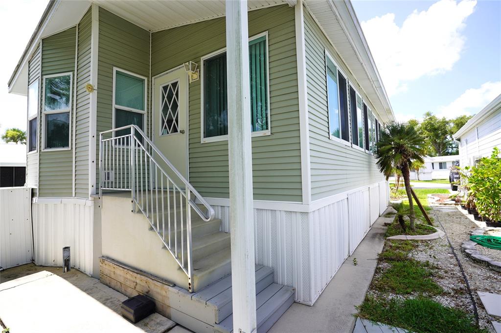 A light green mobile home exterior with white skirting, a front staircase, and metal railings — 125 BROOKSHIRE DRIVE, NOKOMIS, FL