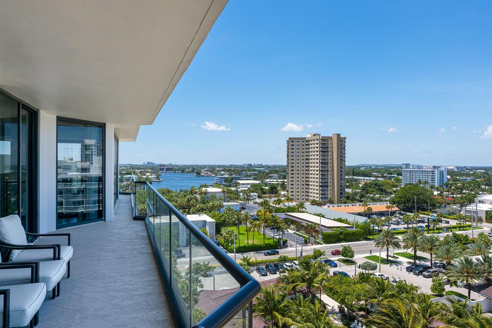 A high-rise balcony with glass railings overlooks a coastal city, palm trees, and a waterway — 1300 S Ocean Boulevard # 906, Pompano Beach FL 33062, POMPANO BEACH, FL