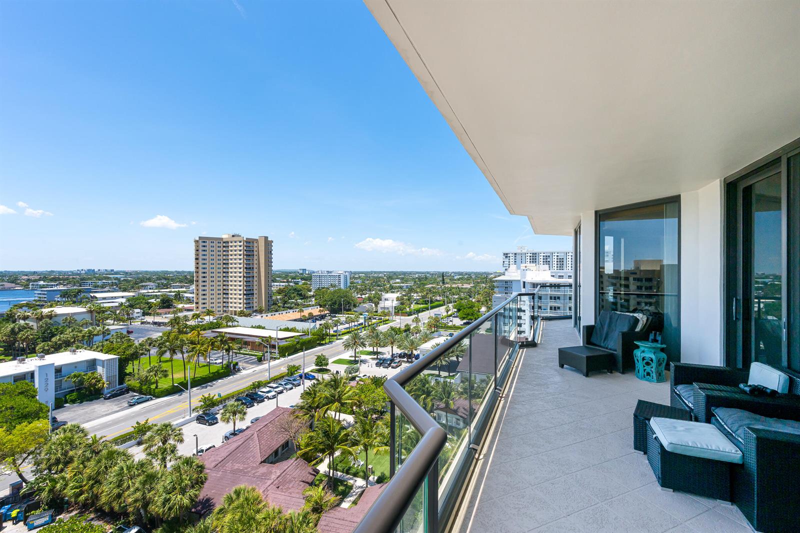 A high-rise balcony with outdoor furniture overlooks a coastal city street and palm trees — 1300 S Ocean Boulevard # 906, Pompano Beach FL 33062, POMPANO BEACH, FL