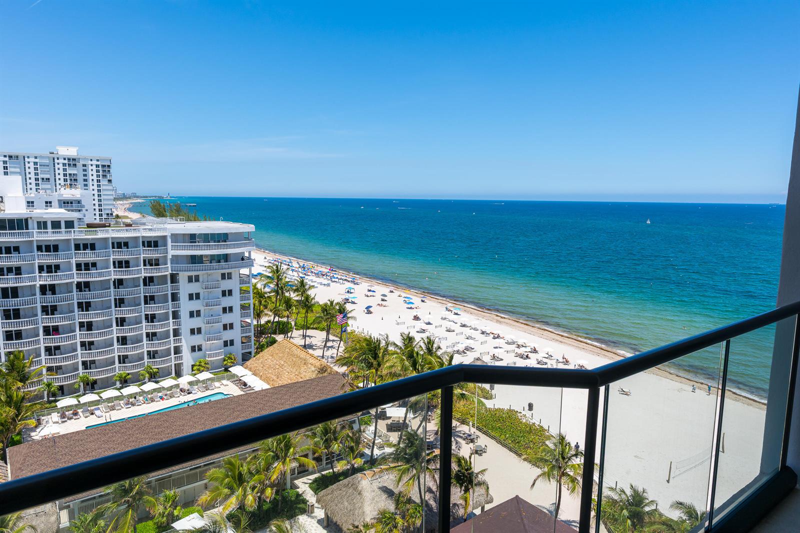A high-angle view from a balcony overlooking a sandy beach, ocean, and nearby resort buildings — 1300 S Ocean Boulevard # 906, Pompano Beach FL 33062, POMPANO BEACH, FL