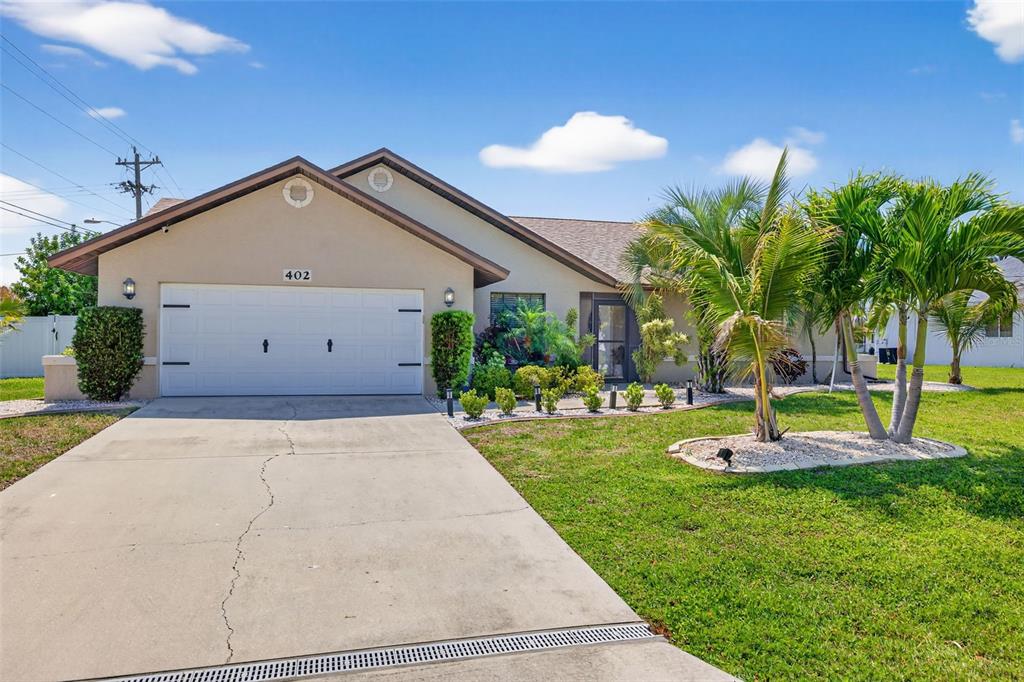 A single-story house with a white garage door, concrete driveway, and palm trees in front — 402 SW 37TH LANE, CAPE CORAL, FL