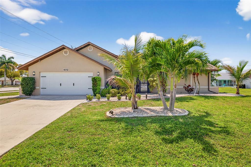 A single-story house with a white garage door, tan stucco exterior, and palm trees — 402 SW 37TH LANE, CAPE CORAL, FL