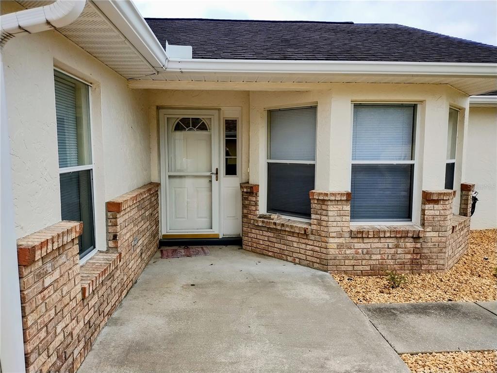 A front entryway with a concrete porch, brick accents, and a white storm door — 9013 SW 91ST CIRCLE, OCALA, FL