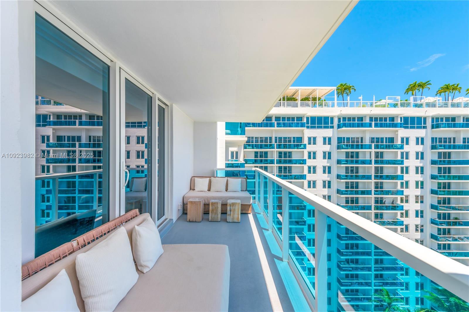 A balcony with outdoor seating overlooks a large, modern apartment complex under a clear sky — 102 24th St # 1544, Miami Beach FL 33139, MIAMI BEACH, FL