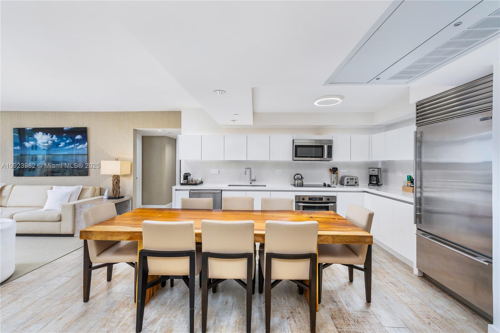 A modern kitchen features white cabinetry, stainless steel appliances, and a large wooden dining table — 102 24th St # 1544, Miami Beach FL 33139, MIAMI BEACH, FL