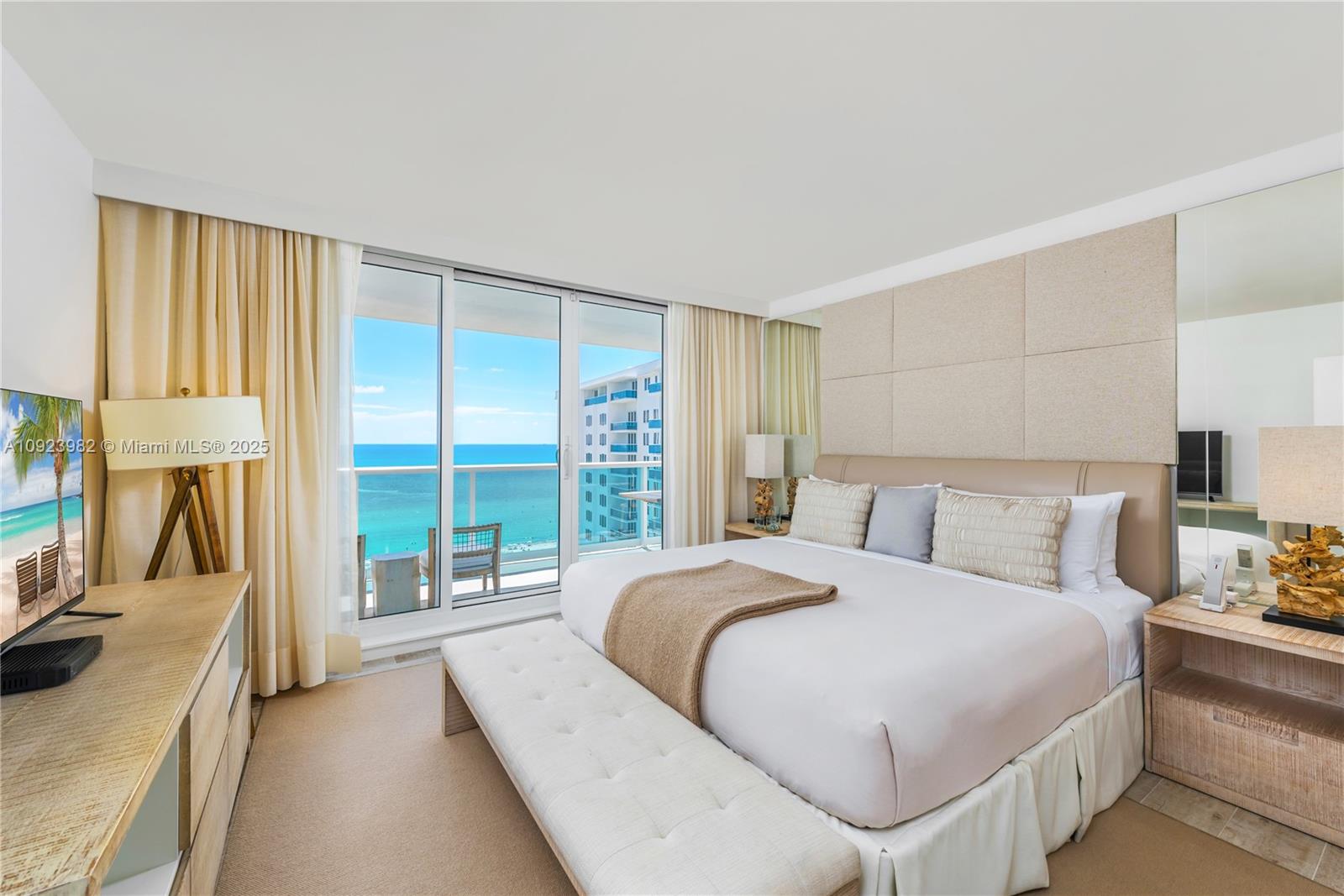 A bedroom features a king bed, a neutral color palette, and a balcony overlooking the ocean — 102 24th St # 1544, Miami Beach FL 33139, MIAMI BEACH, FL