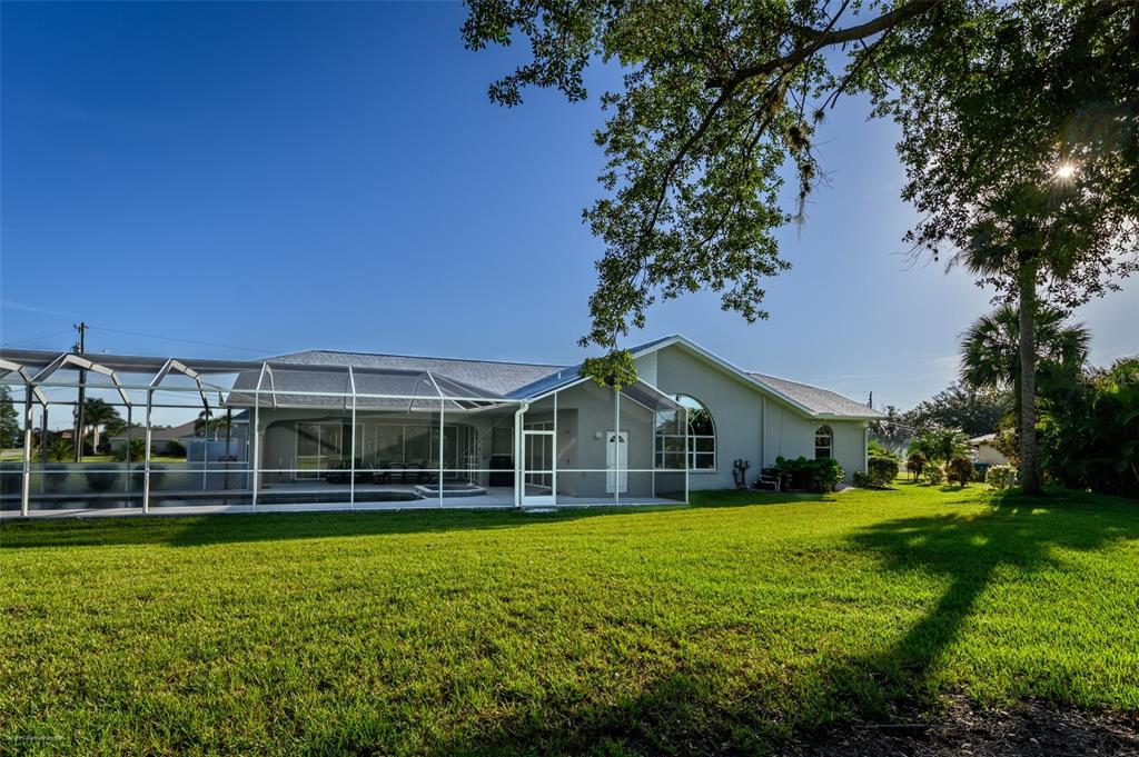 A view of the back of a house with a screened-in pool enclosure and lawn — 27406 TIERRA DEL FUEGO CIRCLE, PUNTA GORDA, FL
