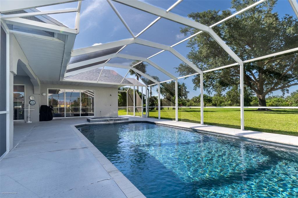 A swimming pool and spa are enclosed within a screened lanai behind a house — 27406 TIERRA DEL FUEGO CIRCLE, PUNTA GORDA, FL