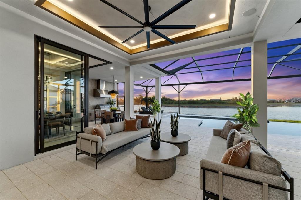 A covered outdoor patio features two sofas, round coffee tables, and a view of a pool — 11710 BLISSBY STREET, VENICE, FL