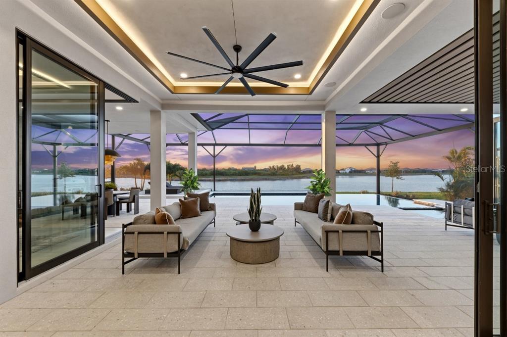 A covered outdoor patio features two sofas, a coffee table, and a pool overlooking water — 11710 BLISSBY STREET, VENICE, FL