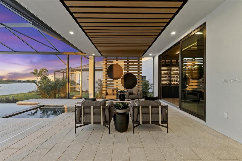 A covered outdoor patio features modern furniture, a slatted wood ceiling, and a swimming pool — 11710 BLISSBY STREET, VENICE, FL