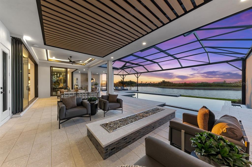 A covered patio features a fire pit, outdoor seating, and a pool overlooking a lake — 11710 BLISSBY STREET, VENICE, FL