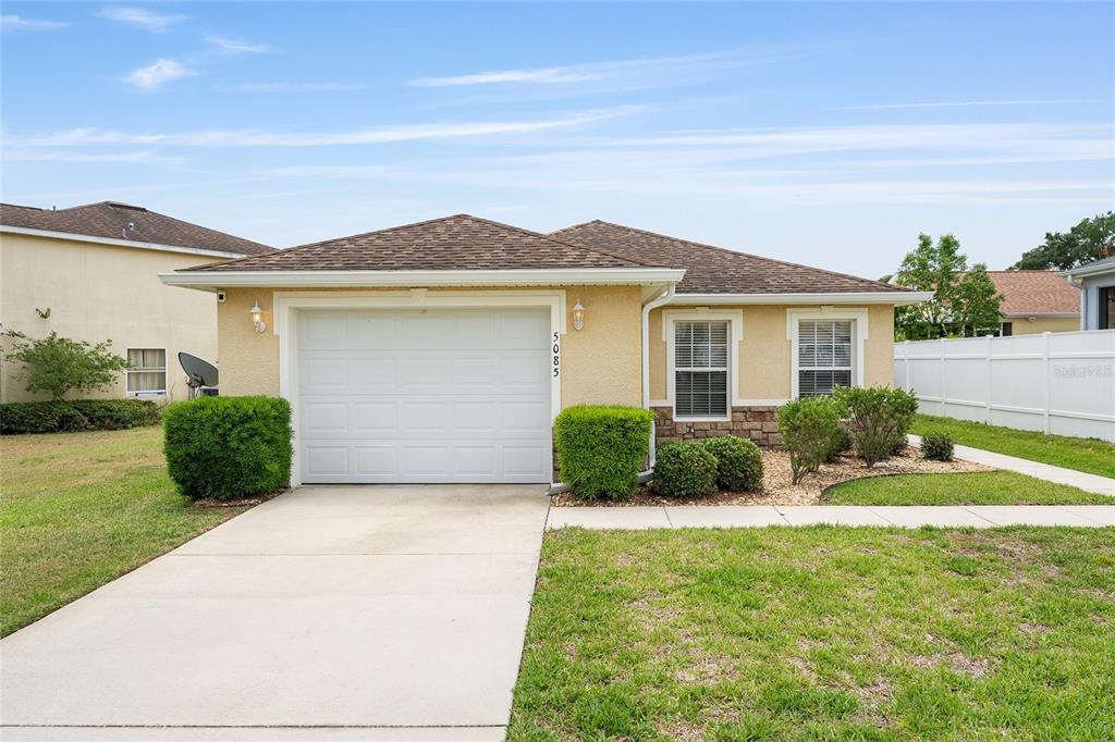 A single-story house with a white garage door, tan stucco siding, and a brown roof — 5085 NE 122ND BOULEVARD, OXFORD, FL