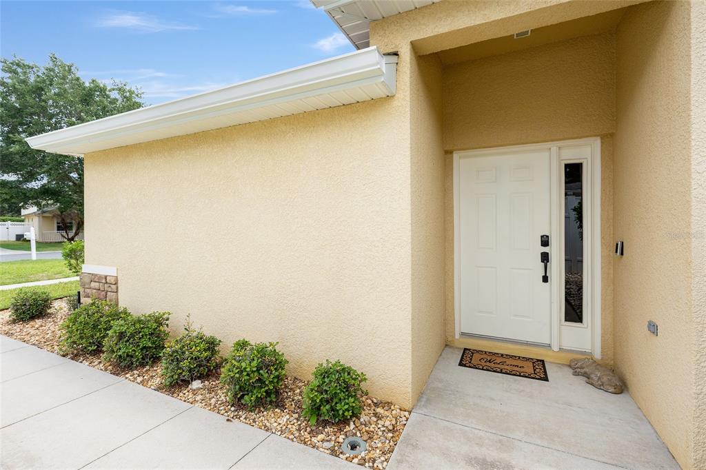 A beige stucco house exterior features a white front door and a small landscaped garden — 5085 NE 122ND BOULEVARD, OXFORD, FL