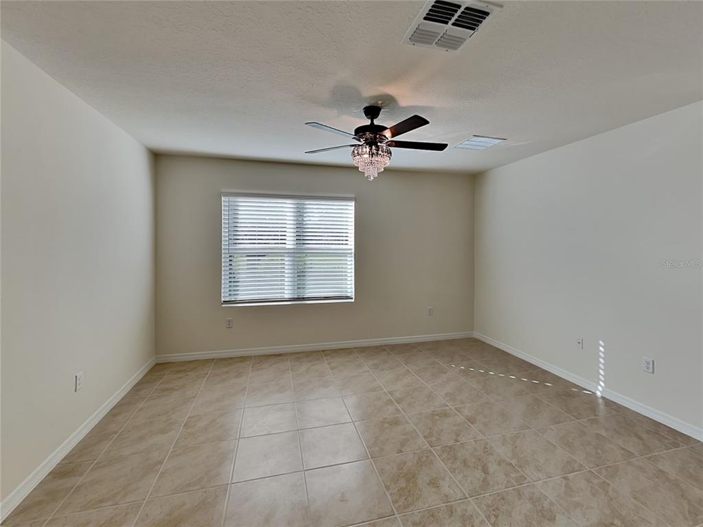 An empty room with beige tile flooring, a ceiling fan with a chandelier, and a window — 1004 BROOKLET DRIVE, DAVENPORT, FL