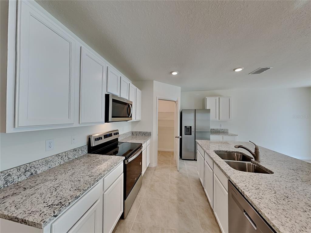 A kitchen features white cabinets, granite countertops, stainless steel appliances, and a central island — 1004 BROOKLET DRIVE, DAVENPORT, FL
