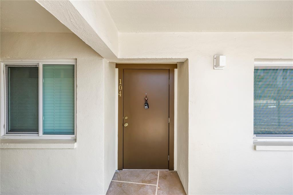 A brown front door with the number 104 is flanked by two windows on a porch — 4435 1ST STREET NE UNIT 104, ST PETERSBURG, FL