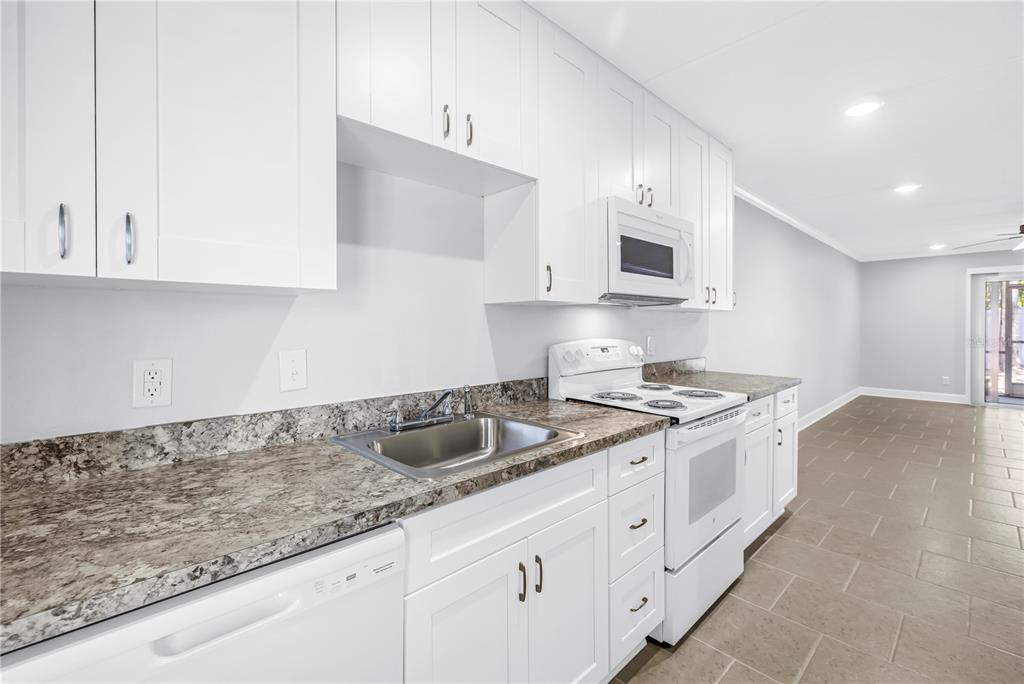 A kitchen features white cabinets, granite countertops, a stainless steel sink, and white appliances — 4435 1ST STREET NE UNIT 104, ST PETERSBURG, FL