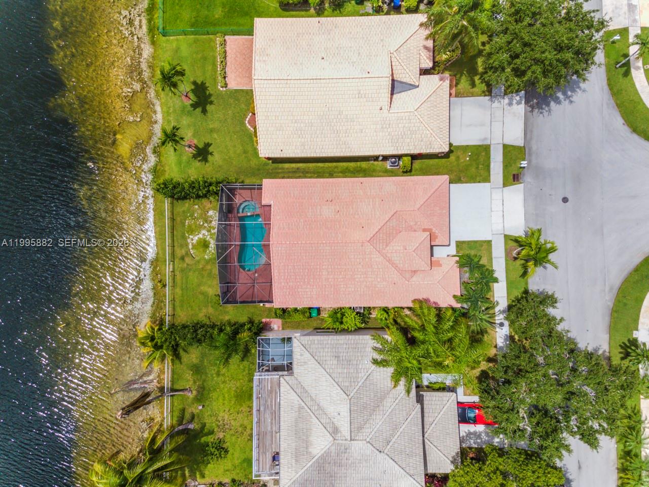 An aerial view shows three waterfront houses with pools and driveways along a curved road — 18096 SW 29th St, Miramar FL 33029, MIRAMAR, FL