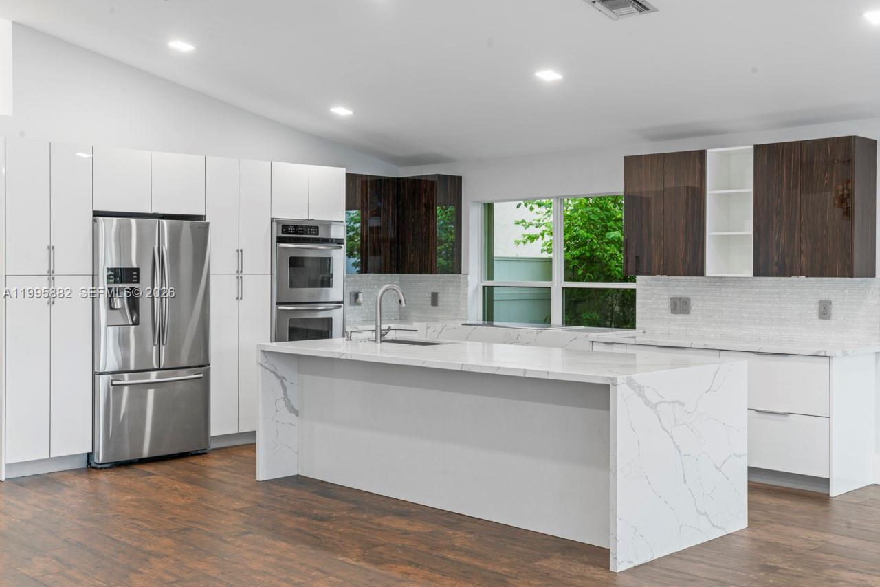A modern kitchen features a white marble island, dark wood upper cabinets, and stainless appliances — 18096 SW 29th St, Miramar FL 33029, MIRAMAR, FL