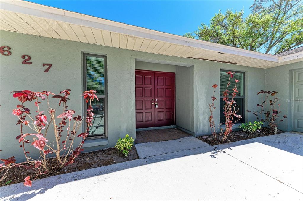 The exterior of a house features a light green facade, a red double door, and landscaping — 627 ALLIGATOR DRIVE, VENICE, FL
