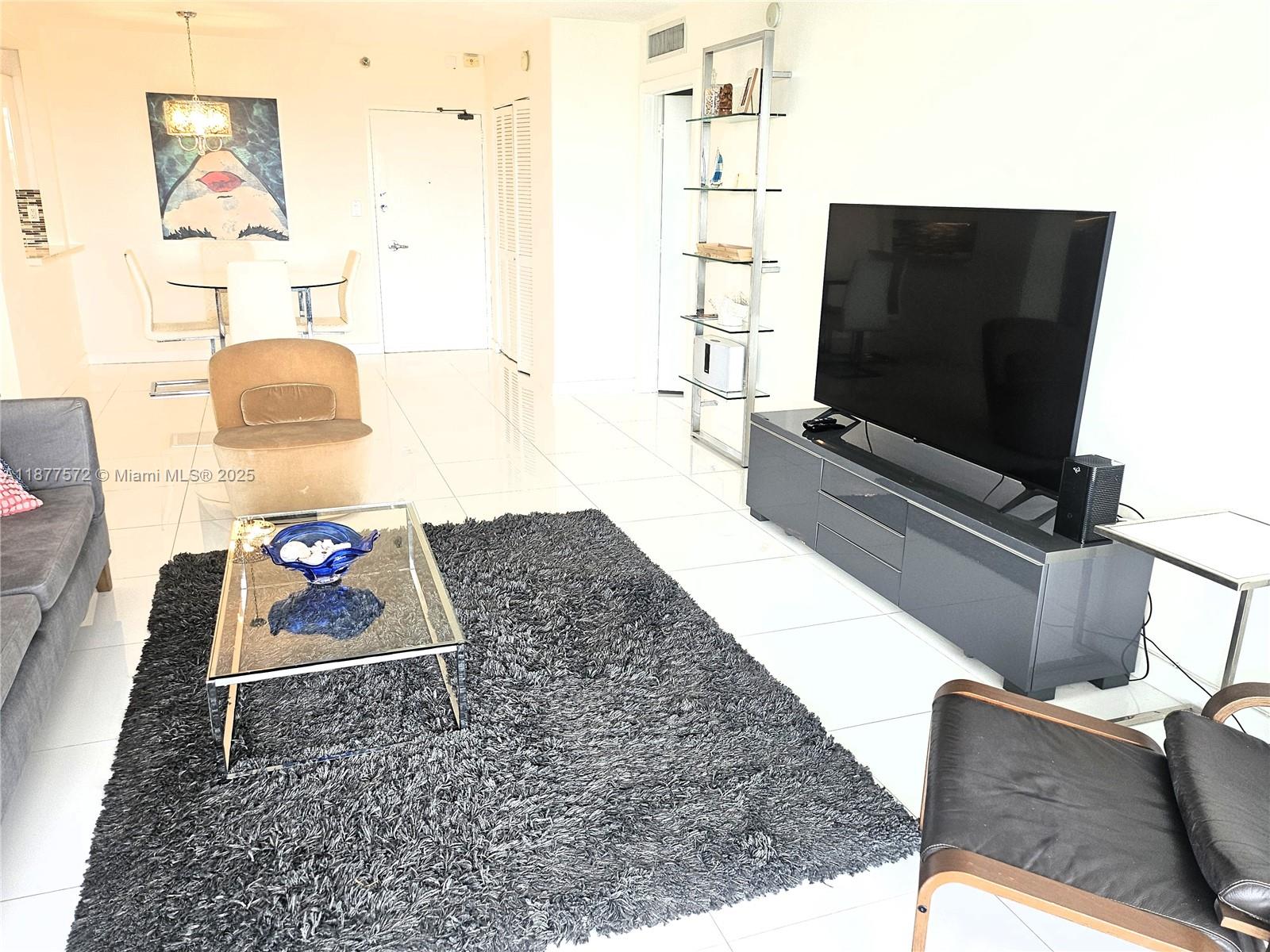 A living room features a large television, a glass coffee table, and a dark rug — 5161 Collins Ave # 707, Miami Beach FL 33140, MIAMI BEACH, FL