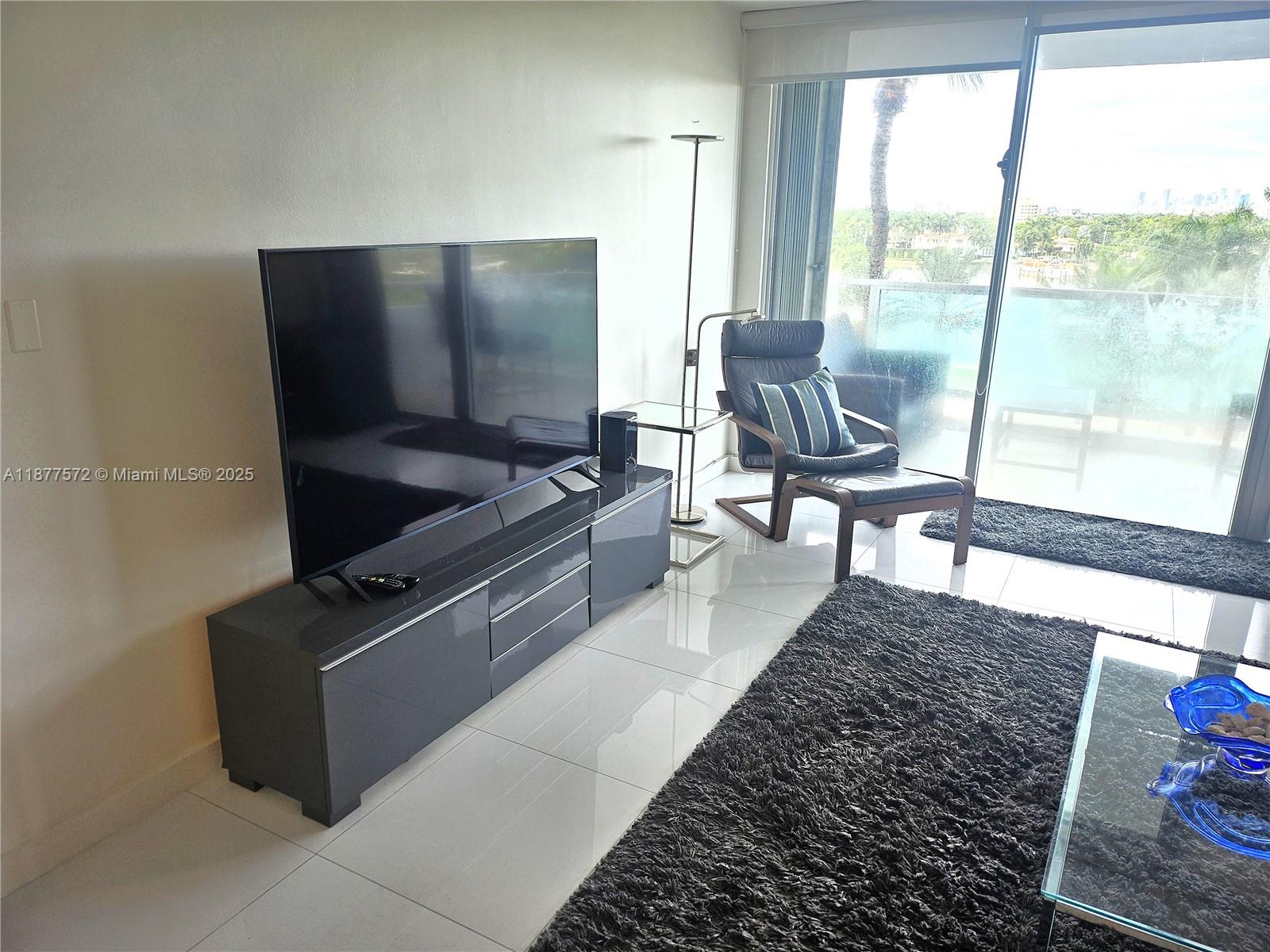 A living room features a large television on a grey console, a leather chair, and balcony — 5161 Collins Ave # 707, Miami Beach FL 33140, MIAMI BEACH, FL