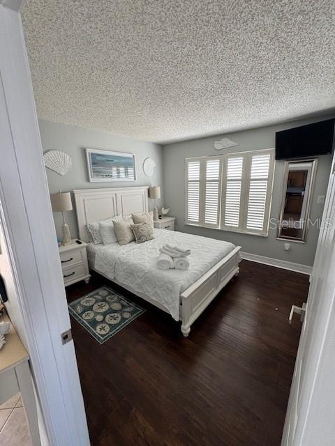 A bedroom features a white bed, dark wood floors, and plantation shutters on the windows — 708 GULF BOULEVARD UNIT D, INDIAN ROCKS BEACH, FL