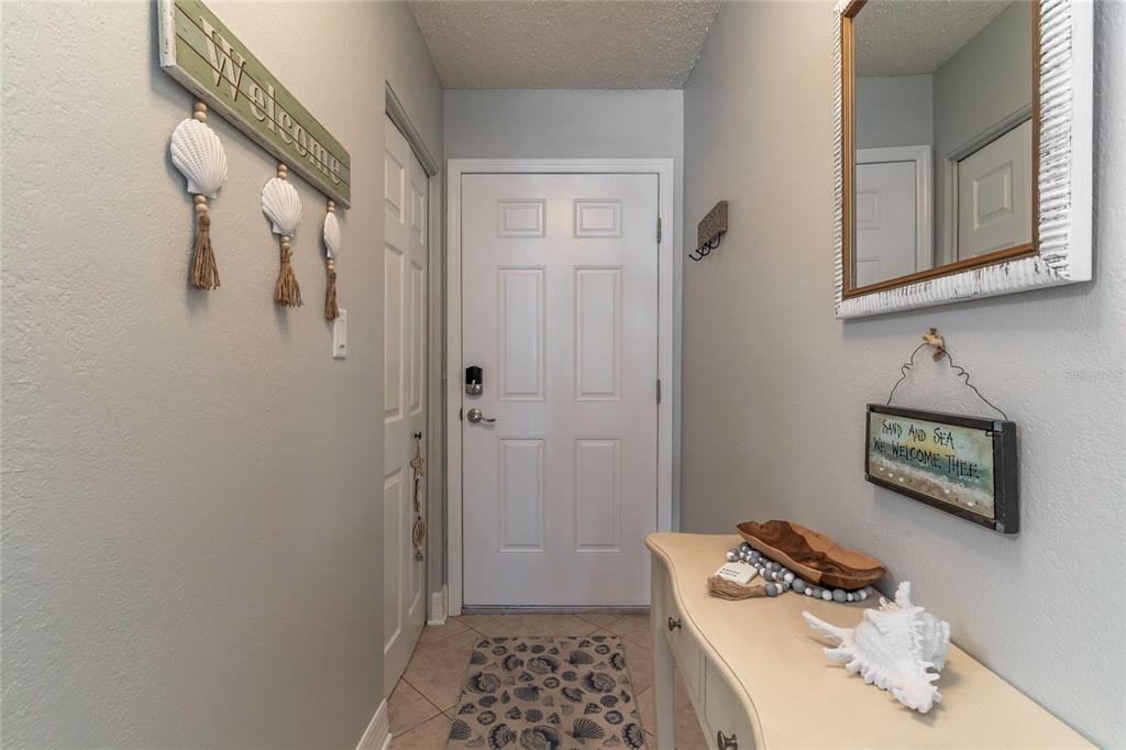 A coastal-themed entryway features a white front door, a console table, and wall-mounted decor — 708 GULF BOULEVARD UNIT D, INDIAN ROCKS BEACH, FL