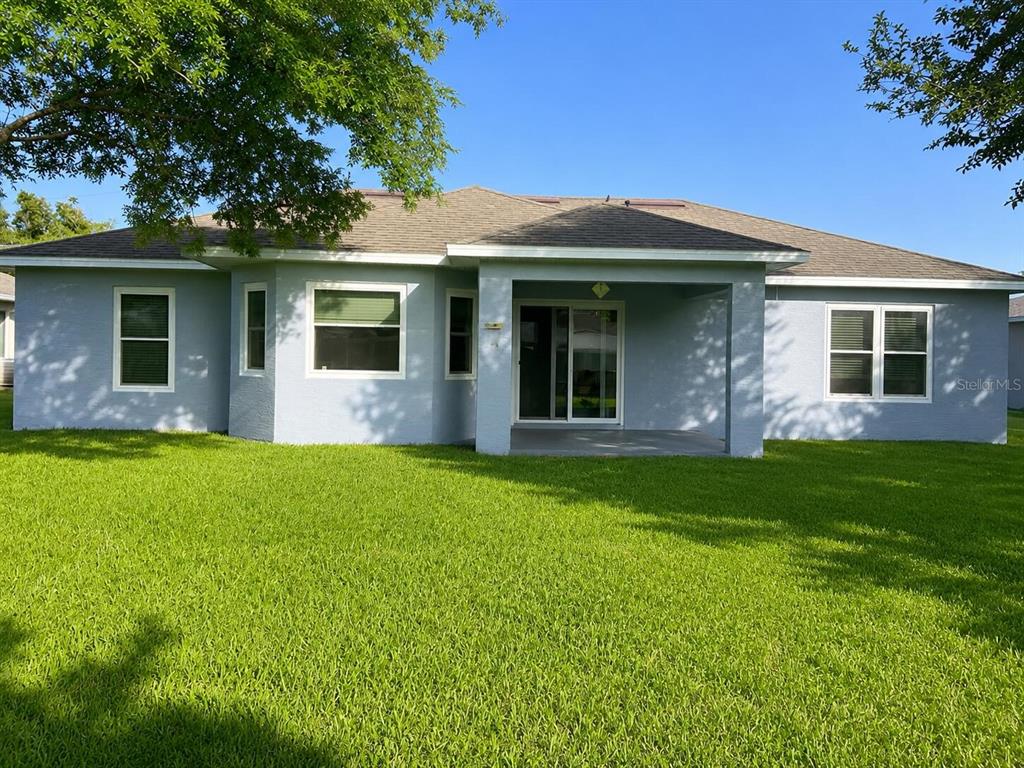 The rear exterior of a single-story house features a covered patio and a grassy lawn — 14 LAMOYNE LANE, PALM COAST, FL