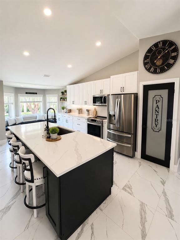 A modern kitchen features a large black island, white cabinetry, stainless appliances, and marble-look flooring — 14 LAMOYNE LANE, PALM COAST, FL