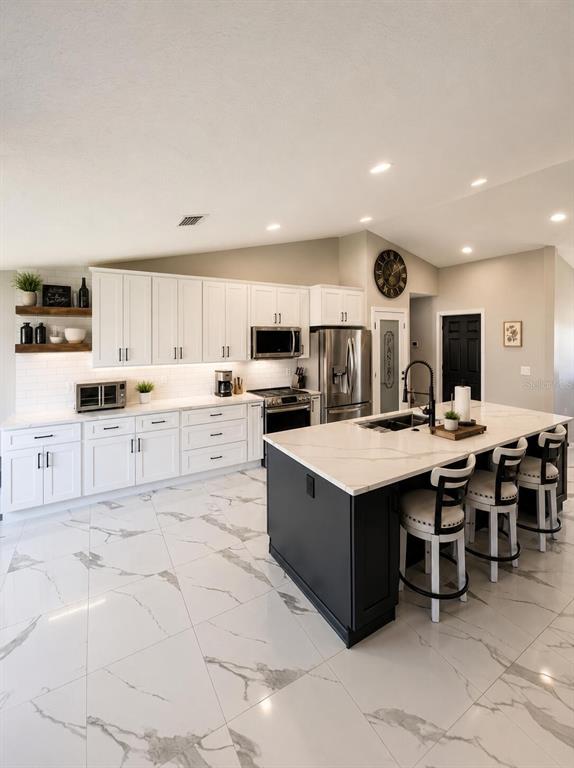 A modern kitchen features white cabinets, a dark island with bar stools, and marble-patterned tile flooring — 14 LAMOYNE LANE, PALM COAST, FL