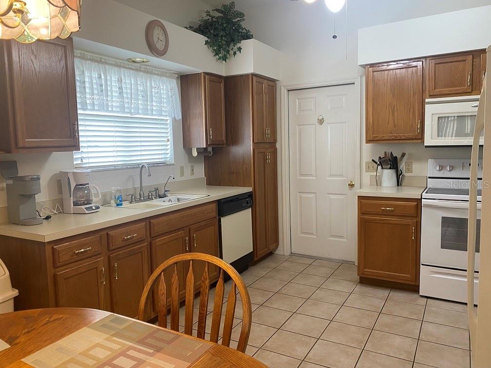 A kitchen with wood cabinets, white appliances, tile flooring, and a window over the sink — 1223 GRANADA COURT, LADY LAKE, FL