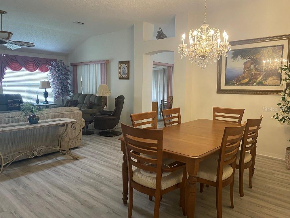 A dining area with a wooden table and chairs sits adjacent to a living room — 1223 GRANADA COURT, LADY LAKE, FL