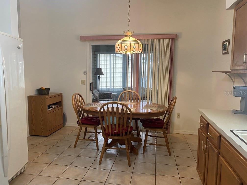 A dining area features a round wooden table, four chairs, tile flooring, and a pendant light — 1223 GRANADA COURT, LADY LAKE, FL