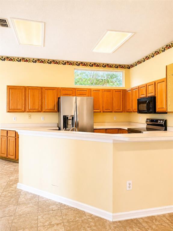 A kitchen features light yellow walls, wooden cabinets, stainless steel appliances, and a breakfast bar — 1995 EMERALD GREEN CIRCLE, OVIEDO, FL