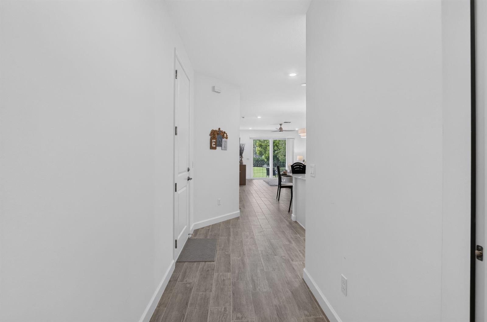 A hallway with wood-look tile flooring leads to an open-concept living area with sliding doors — 13828 Hero Path, Delray Beach FL 33484, DELRAY BEACH, FL