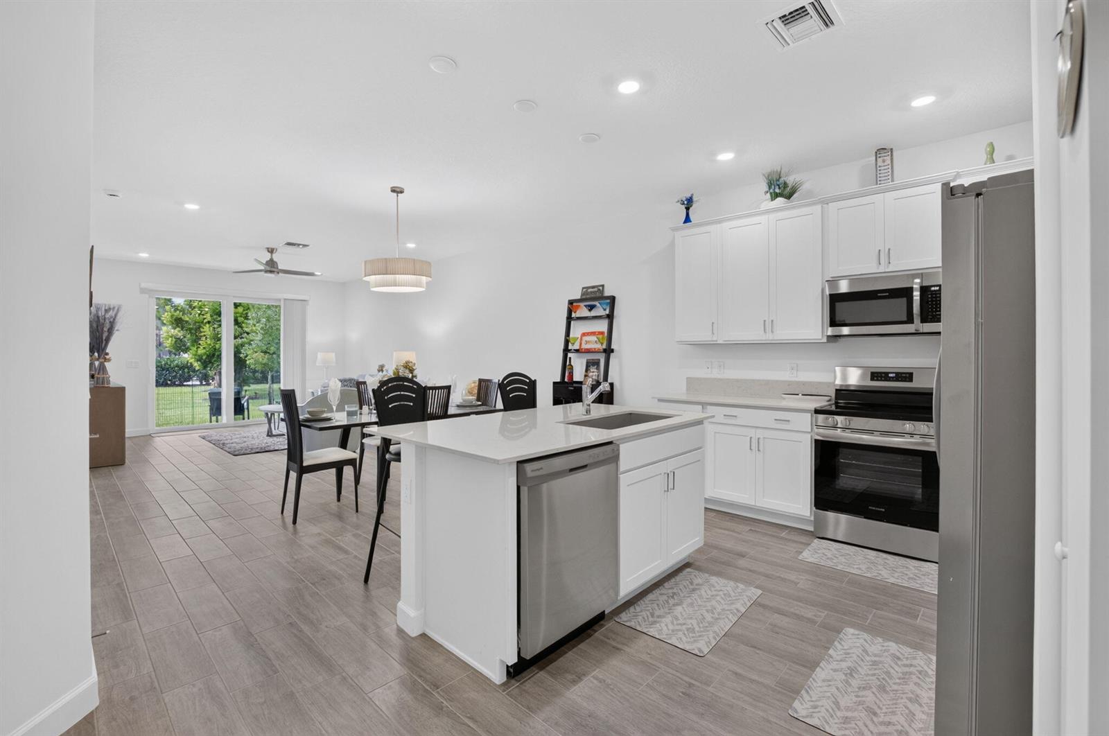 A modern kitchen with white cabinets and a center island opens to a dining area — 13828 Hero Path, Delray Beach FL 33484, DELRAY BEACH, FL